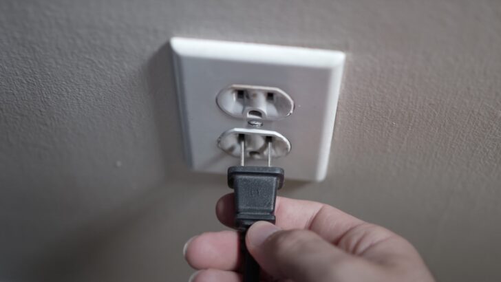 Photo of person unplugging tv power cord from the wall outlet