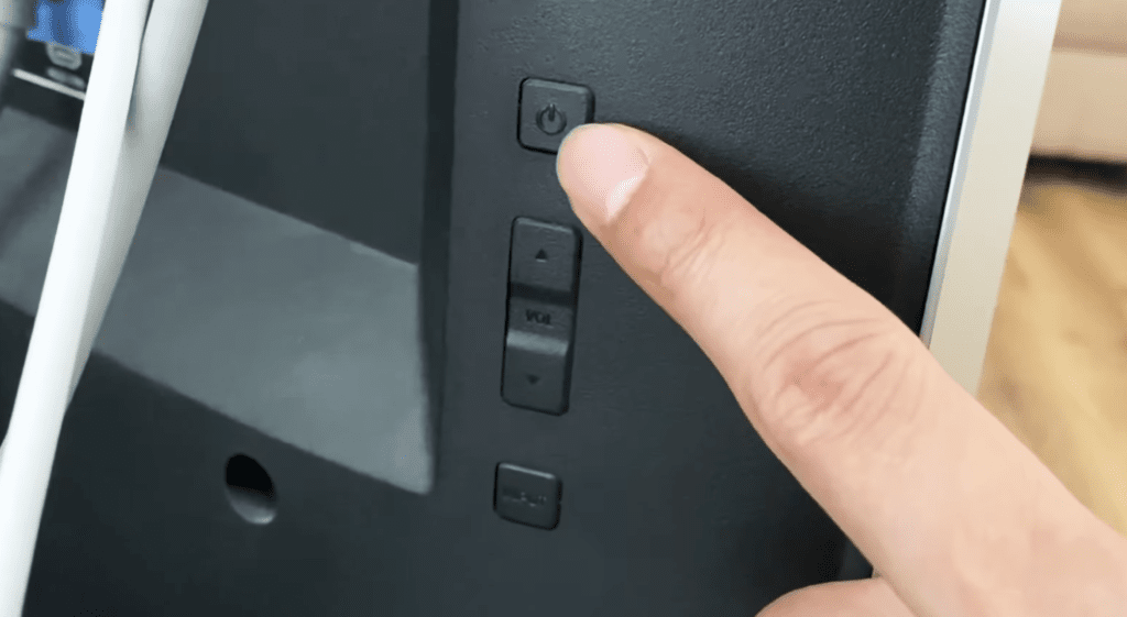 Photo of someone pointing to the power button on the left backside of a Vizio TV