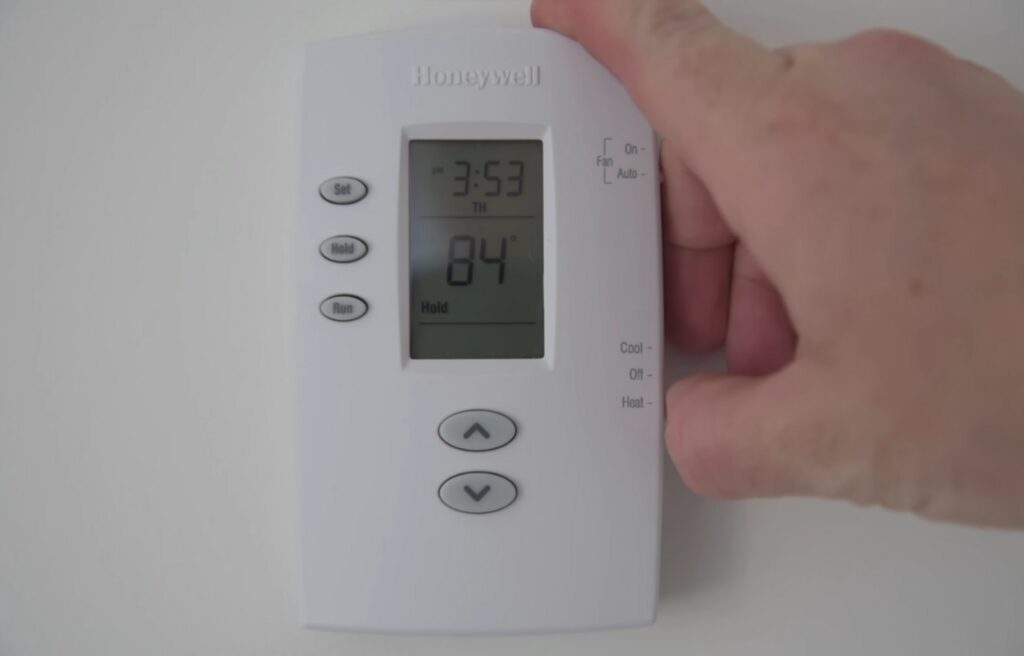 Hand touching a Honeywell 2000 series thermostat