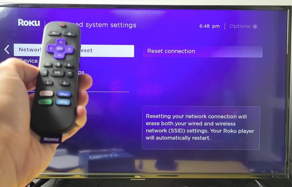 A Roku remote against TV showing reset network connection