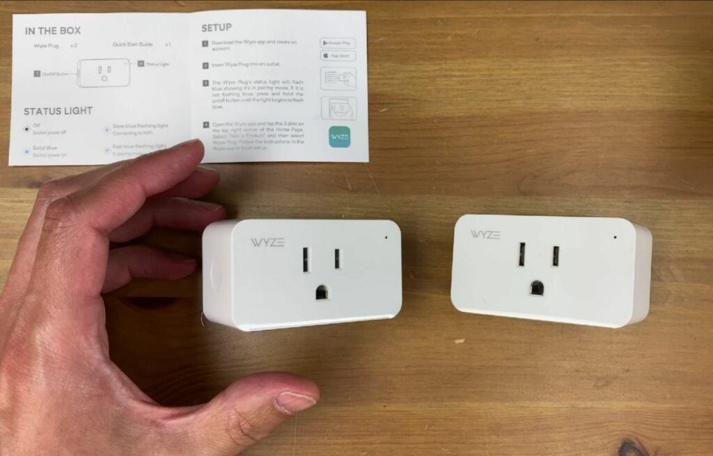 hand holding two Wyze Plugs on a wooden table