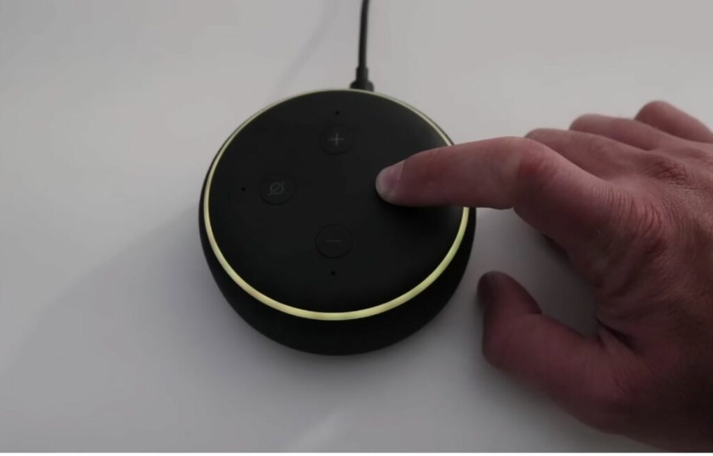 Hand pressing the action button to reset an Alexa echo dot