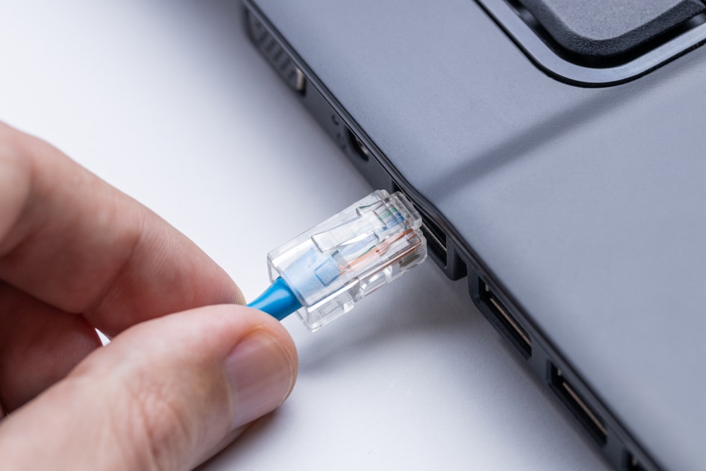 person plugging internet ethernet cable to laptop
